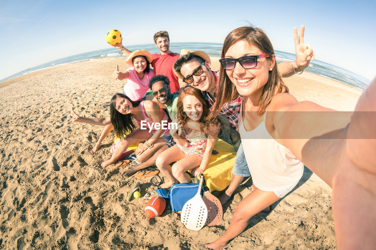 Portrait of smiling young friends taking selfie at beach on sunny day