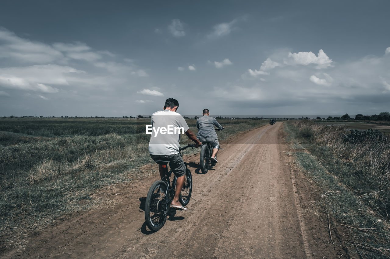 Rear view of man riding bicycle on road against sky