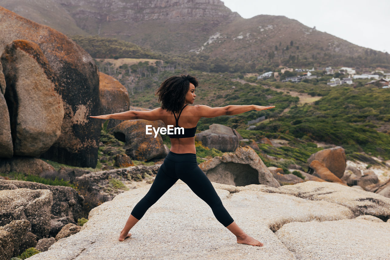 full length of woman stretching while standing on rock