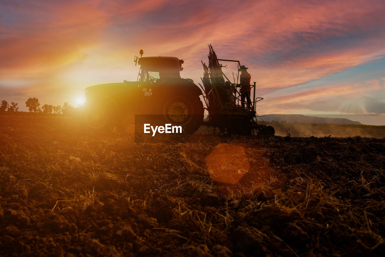 TRACTOR ON FIELD AGAINST SUNSET SKY
