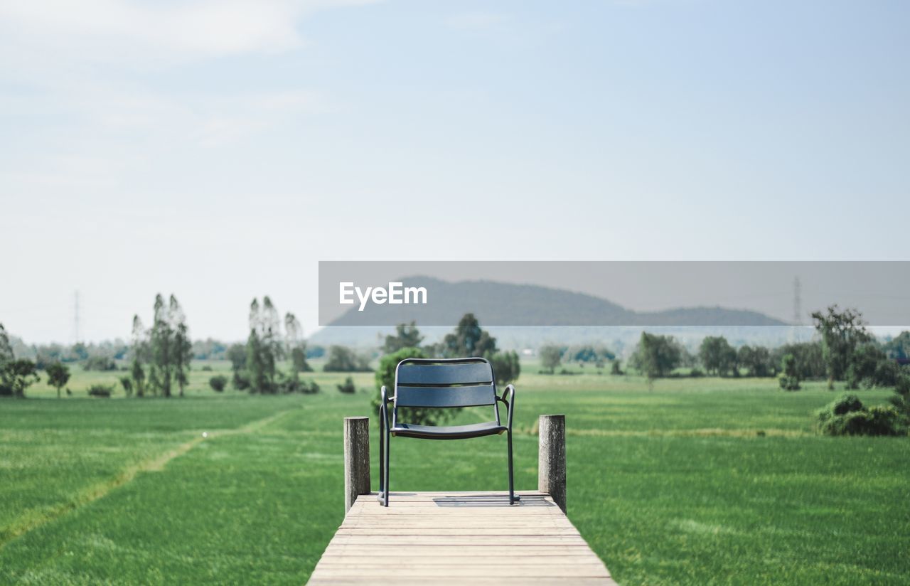 Empty park bench on field against sky