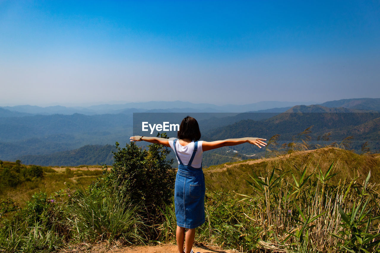 Rear view of woman standing on mountain while looking at landscape against sky