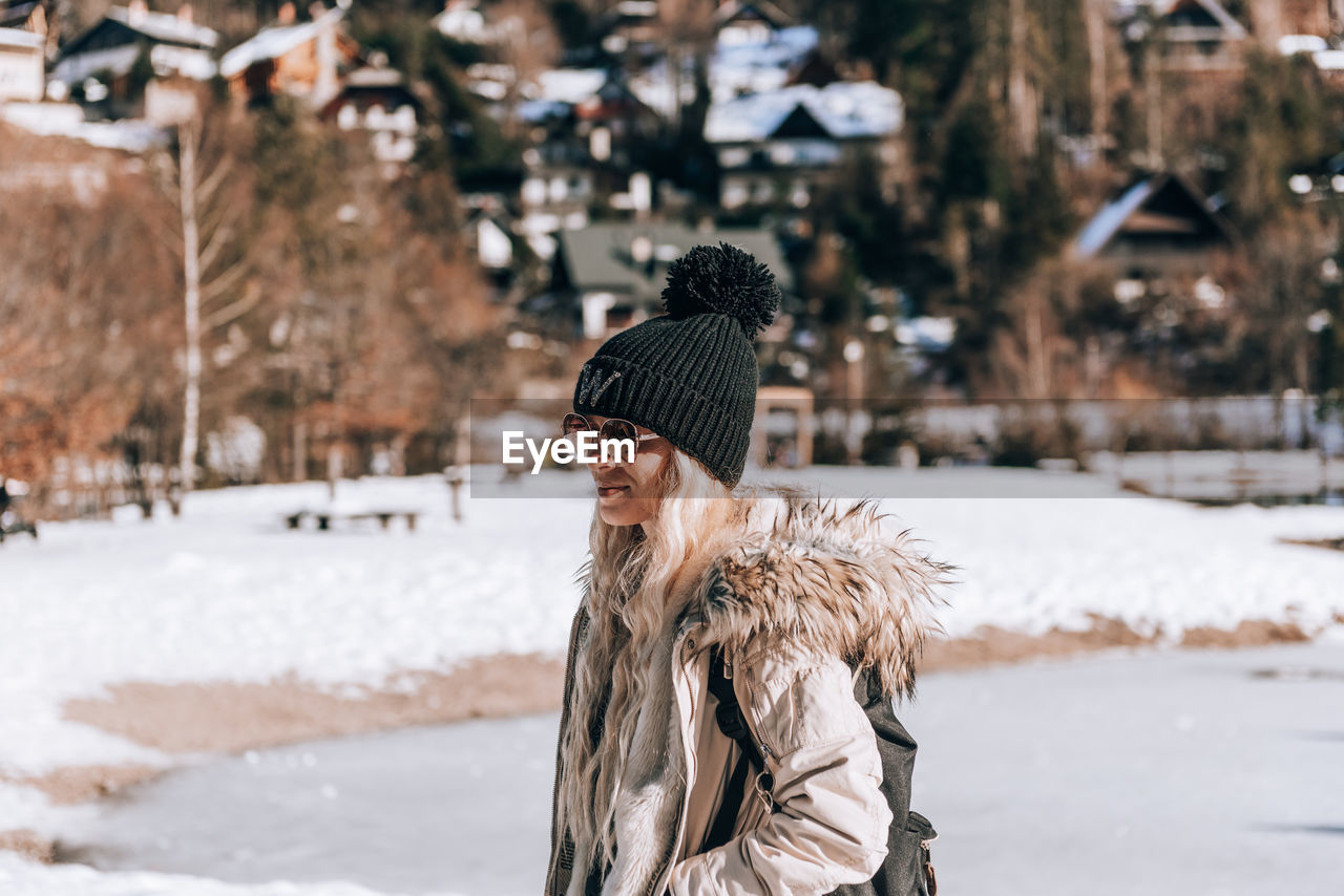 Stylish woman with blond hair, wearing winter clothes, standing on shore of lake jasna in slovenia