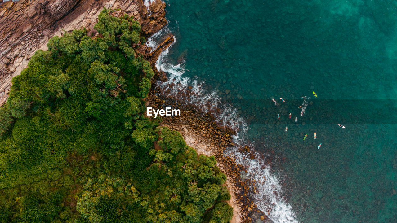 Tropical coast, surfers, ocean and waves crashing against rocks, drone shot, exotic landscape.