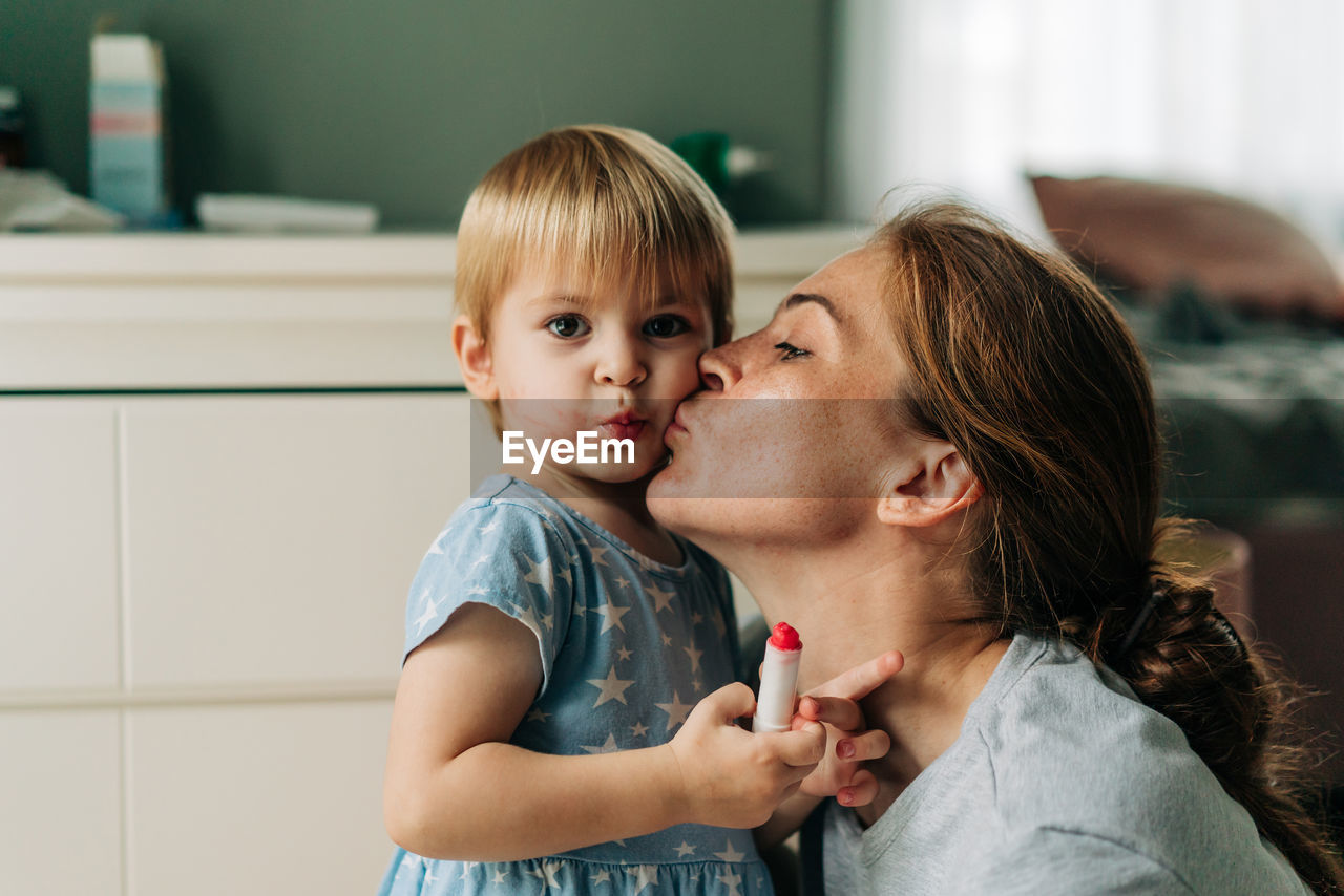 Mom kisses a little funny toddler girl.