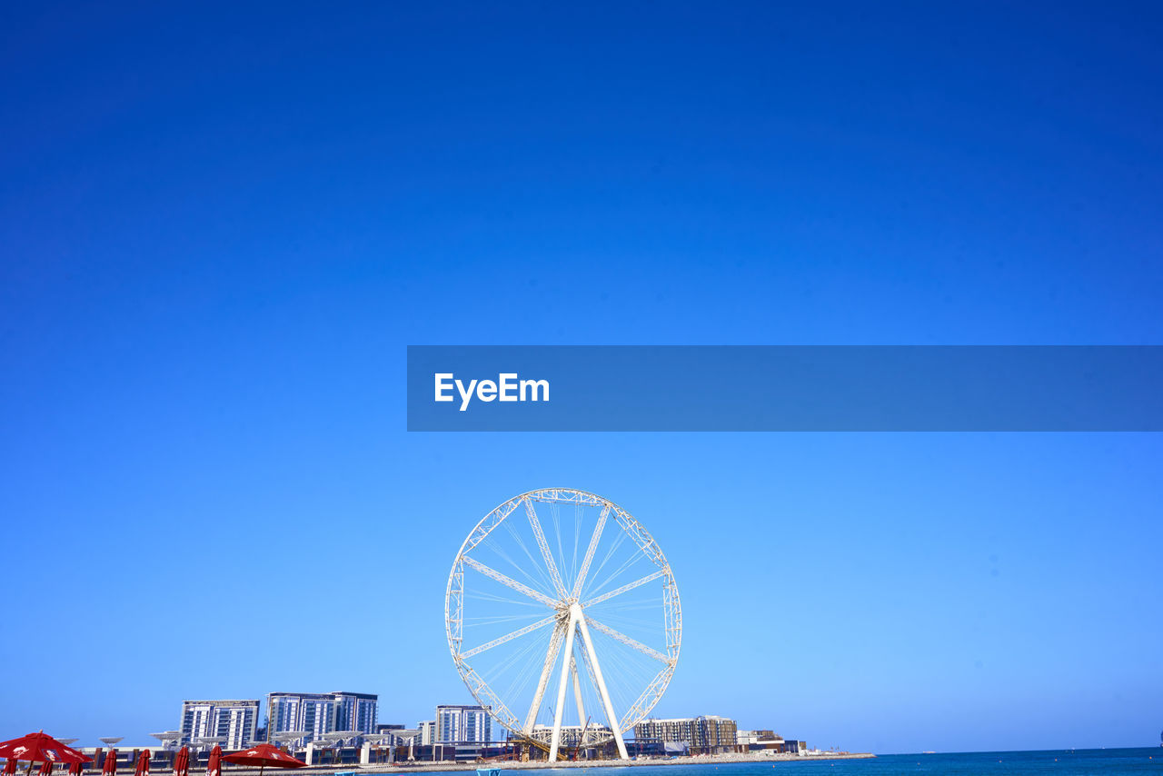 Ferris wheel and buildings against clear blue sky