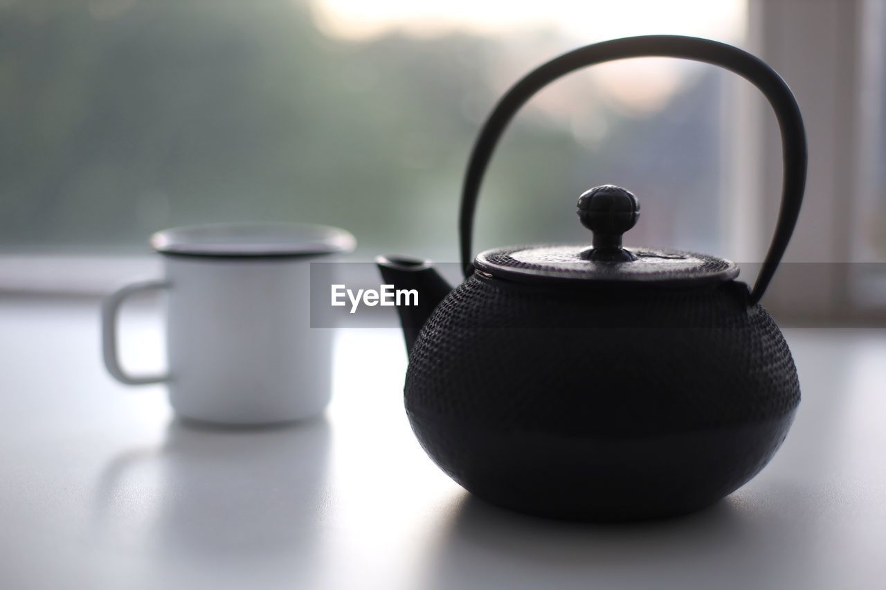 teapot, kettle, tea, hot drink, food and drink, drink, tea kettle, stovetop kettle, cup, indoors, tea cup, mug, no people, household equipment, refreshment, kitchen utensil, home appliance, still life, handle, ceramic, domestic room, food, close-up, table, crockery, simplicity, black, focus on foreground, tableware, small appliance, steam, afternoon tea, iron