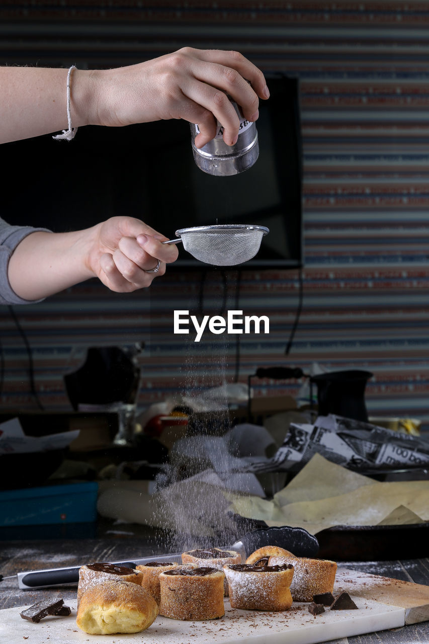 Cropped image of man dusting powdered sugar on dessert in kitchen