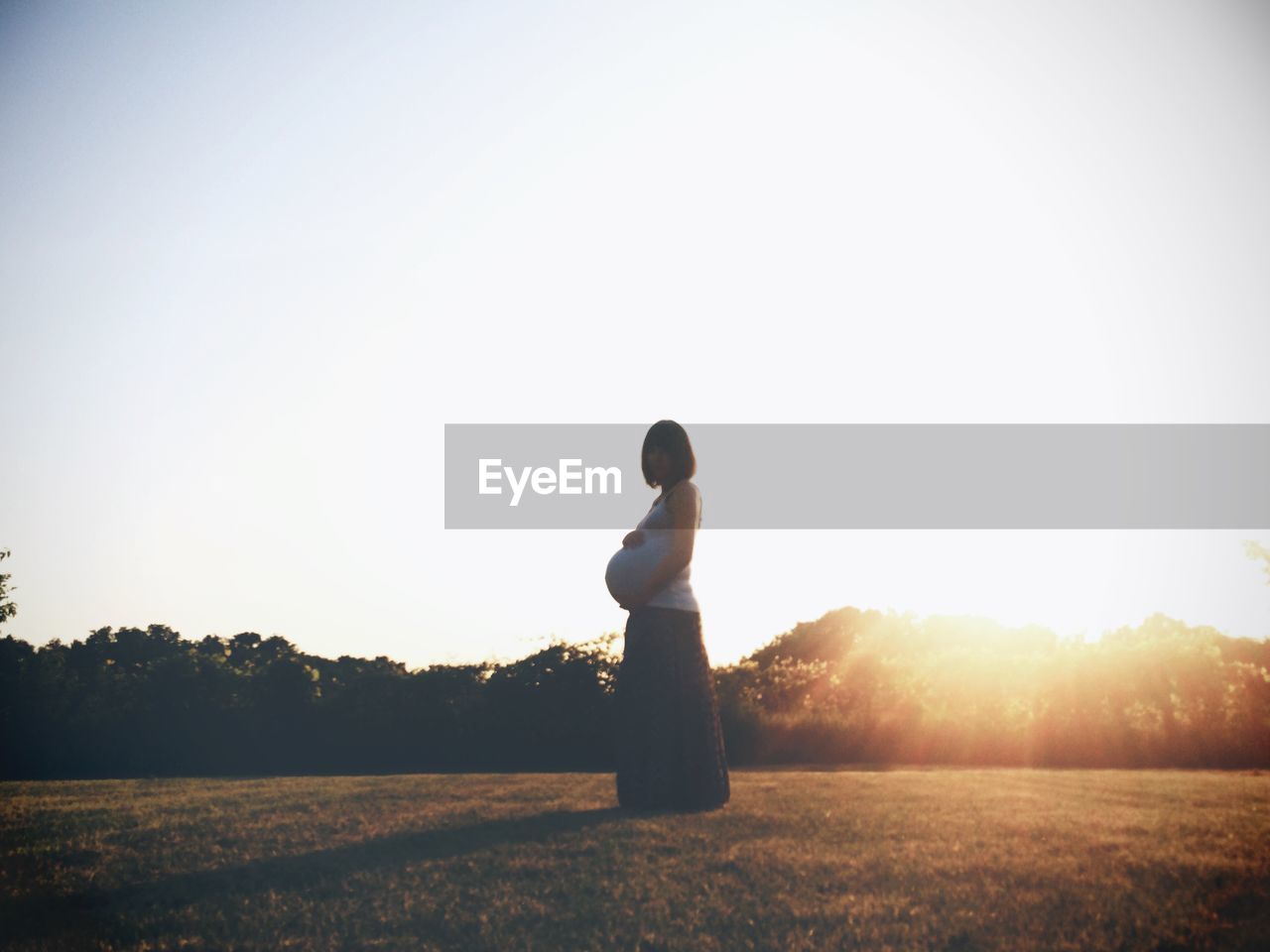 Side view of pregnant woman standing on land against clear sky