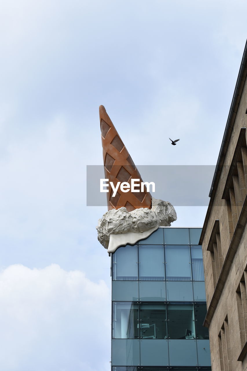 Low angle view of bird flying over building against cloudy sky