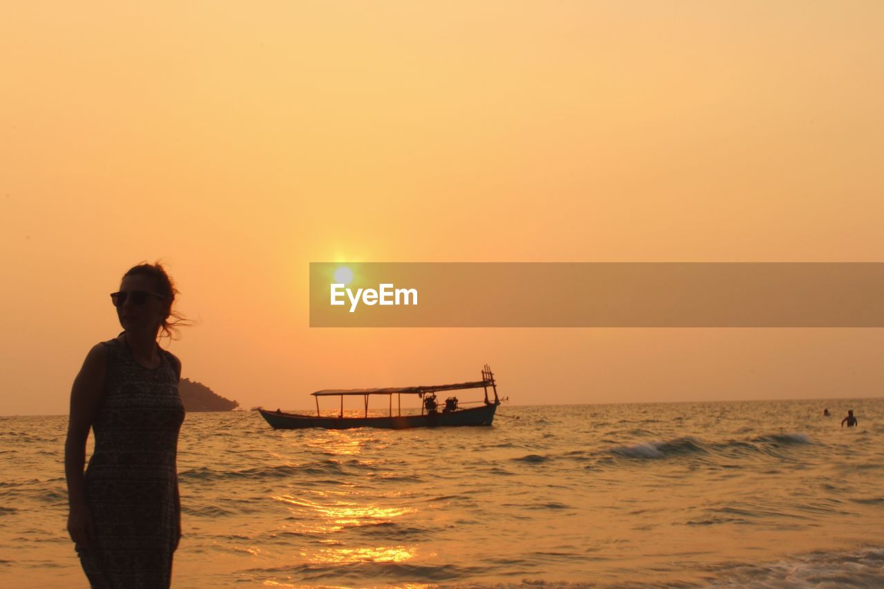 Woman standing by sea against sky during sunset