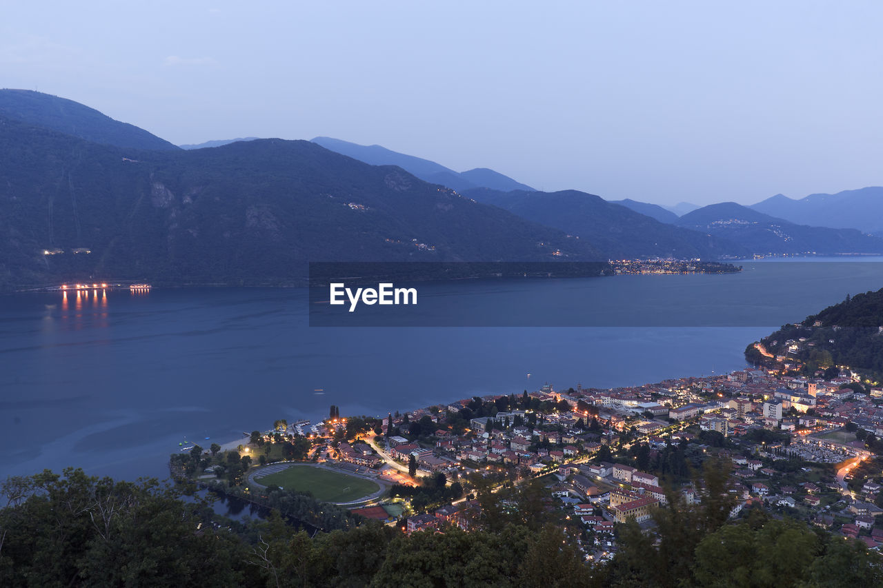 High angle view of illuminated city by sea against sky