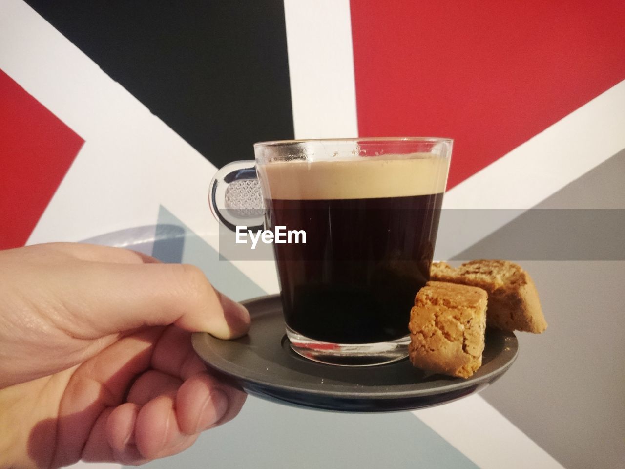 Cropped hand of person holding black coffee with biscotti in plate