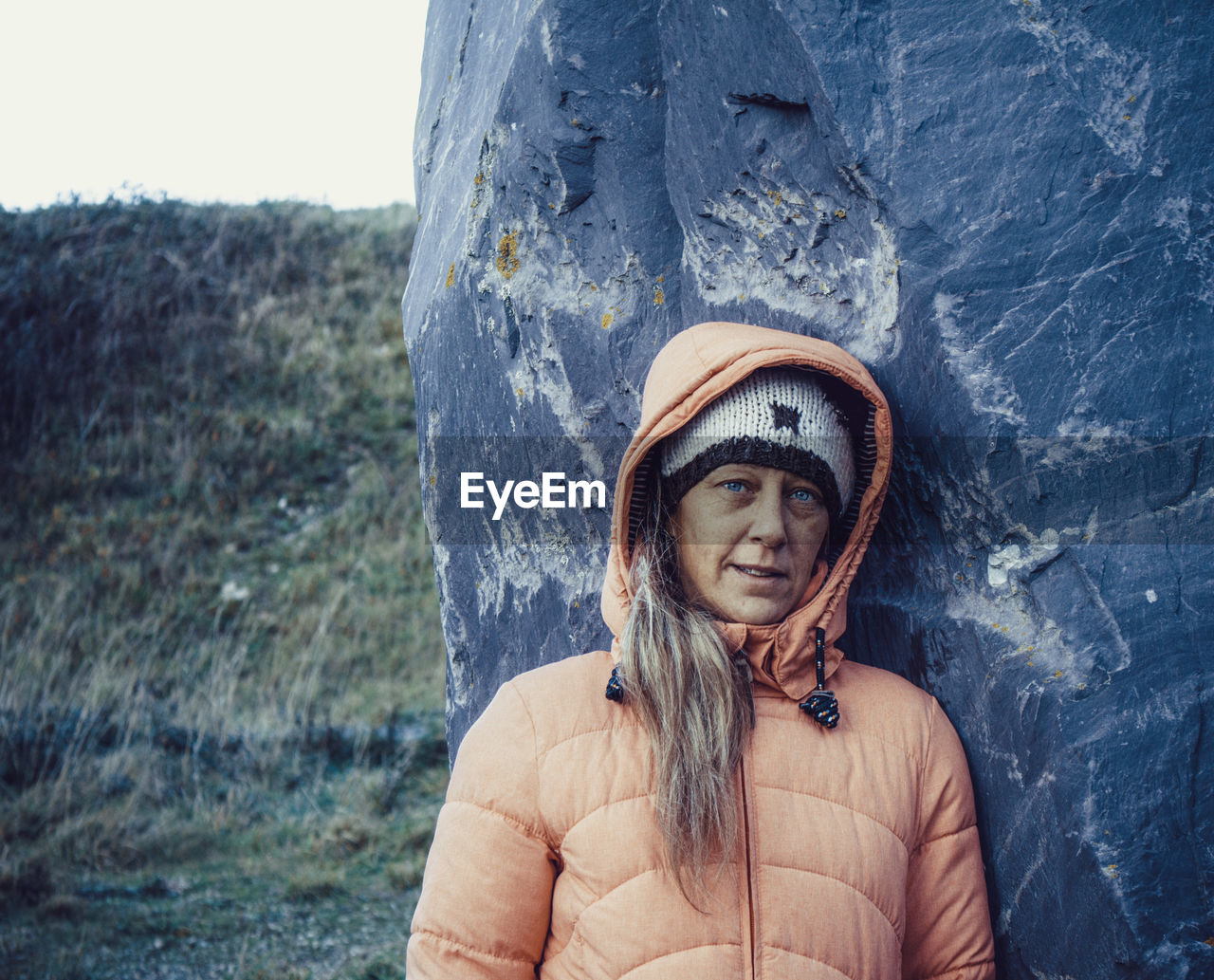 Portrait of woman in warm clothing standing against rock