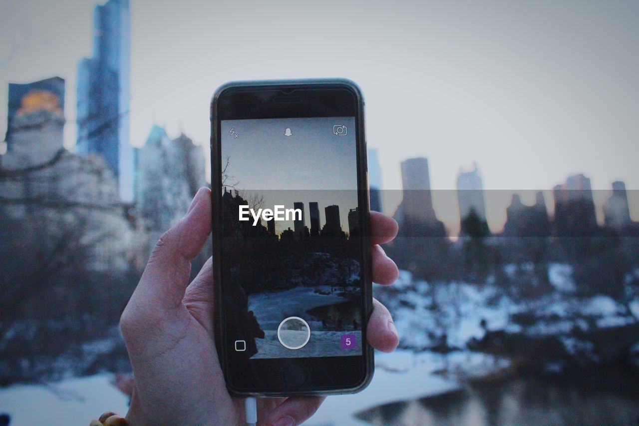 Cropped image of hand photographing cityscape with smart phone during winter