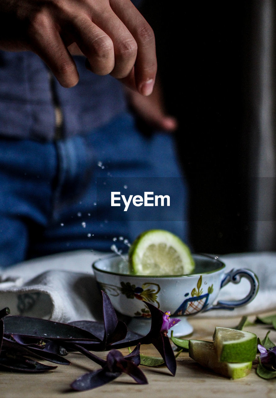 Cropped image of hand throwing lemon slice in cup