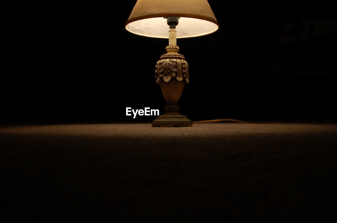 Close-up of illuminated lamp on table against black background