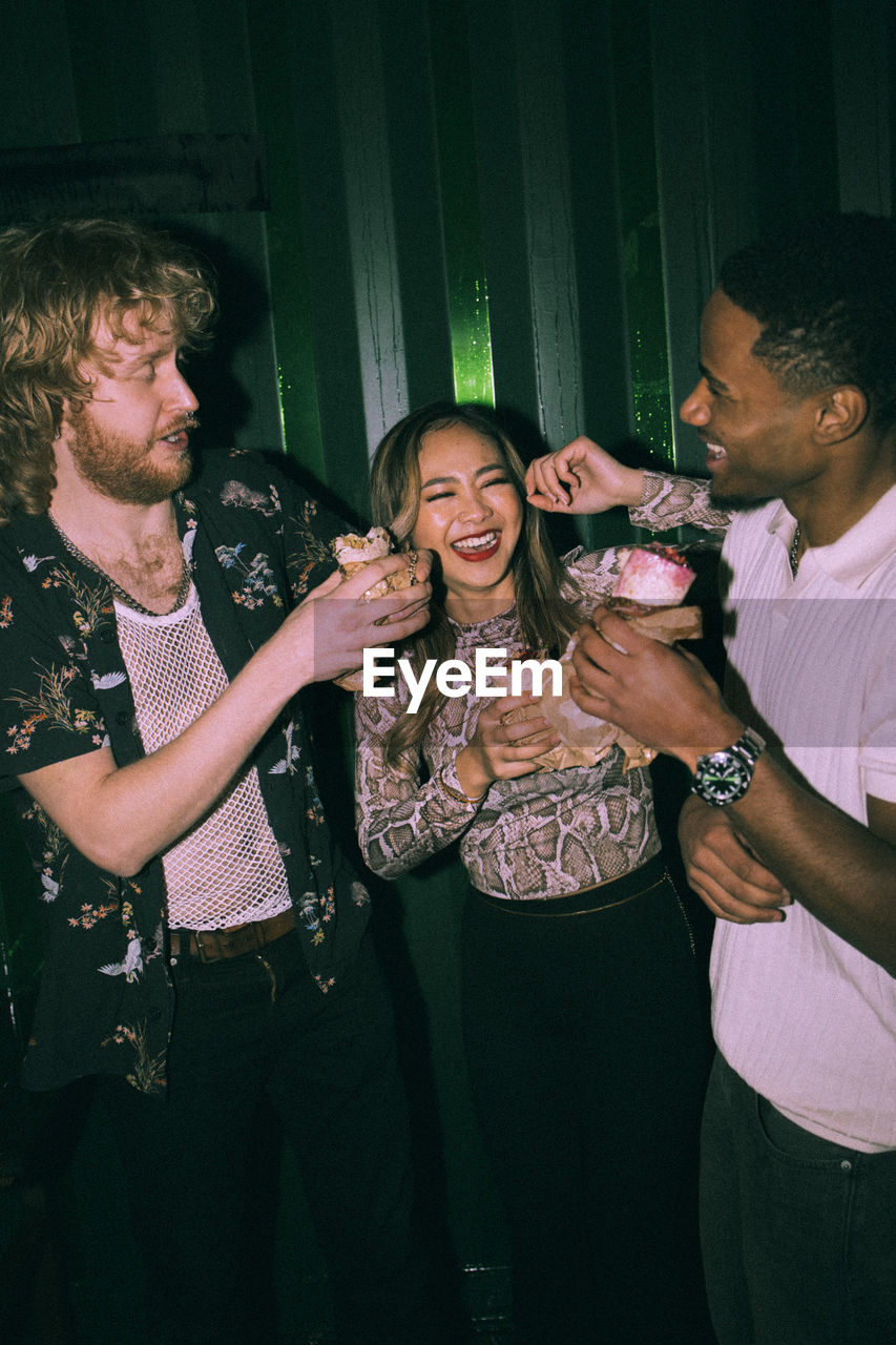 Cheerful young multiracial friends eating wrap sandwiches together at nightclub