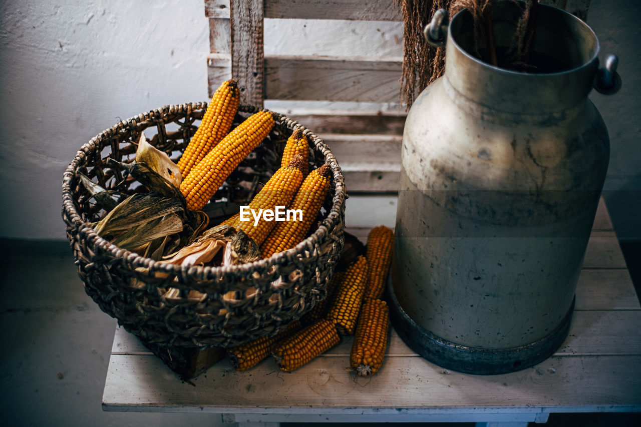 Corn in basket near metal milk jug on table