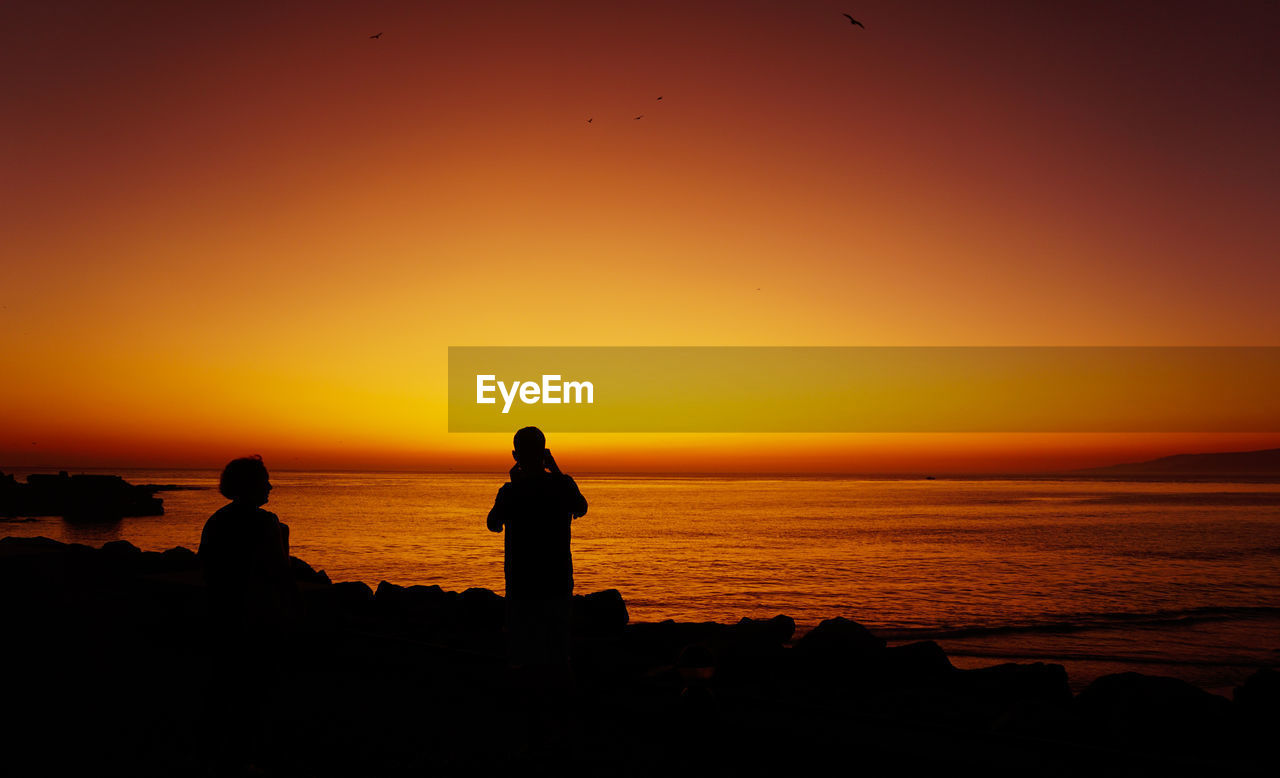 SILHOUETTE MAN LOOKING AT SEA DURING SUNSET