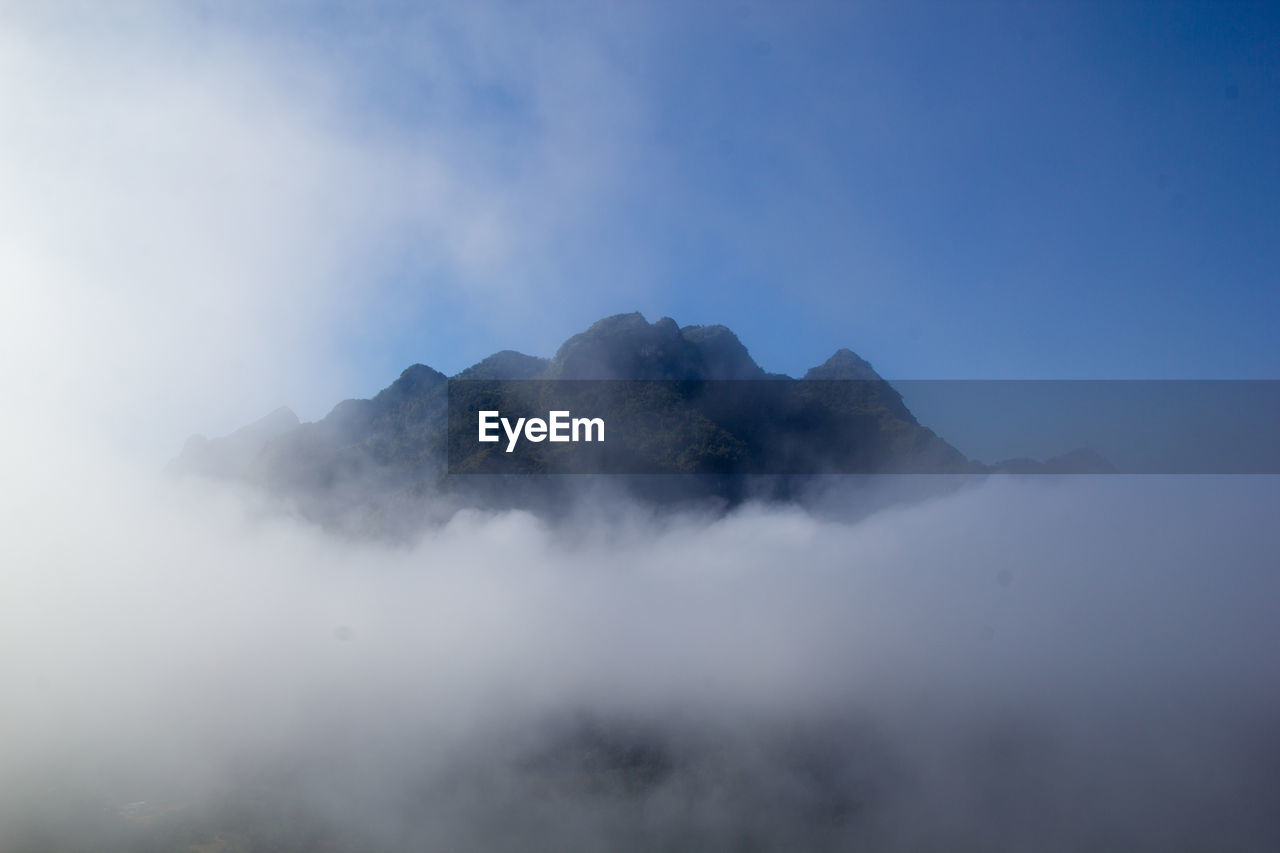 SCENIC VIEW OF FOG COVERING MOUNTAIN AGAINST SKY