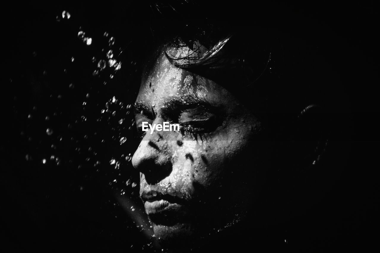 Close-up of water splashing on young man against black background