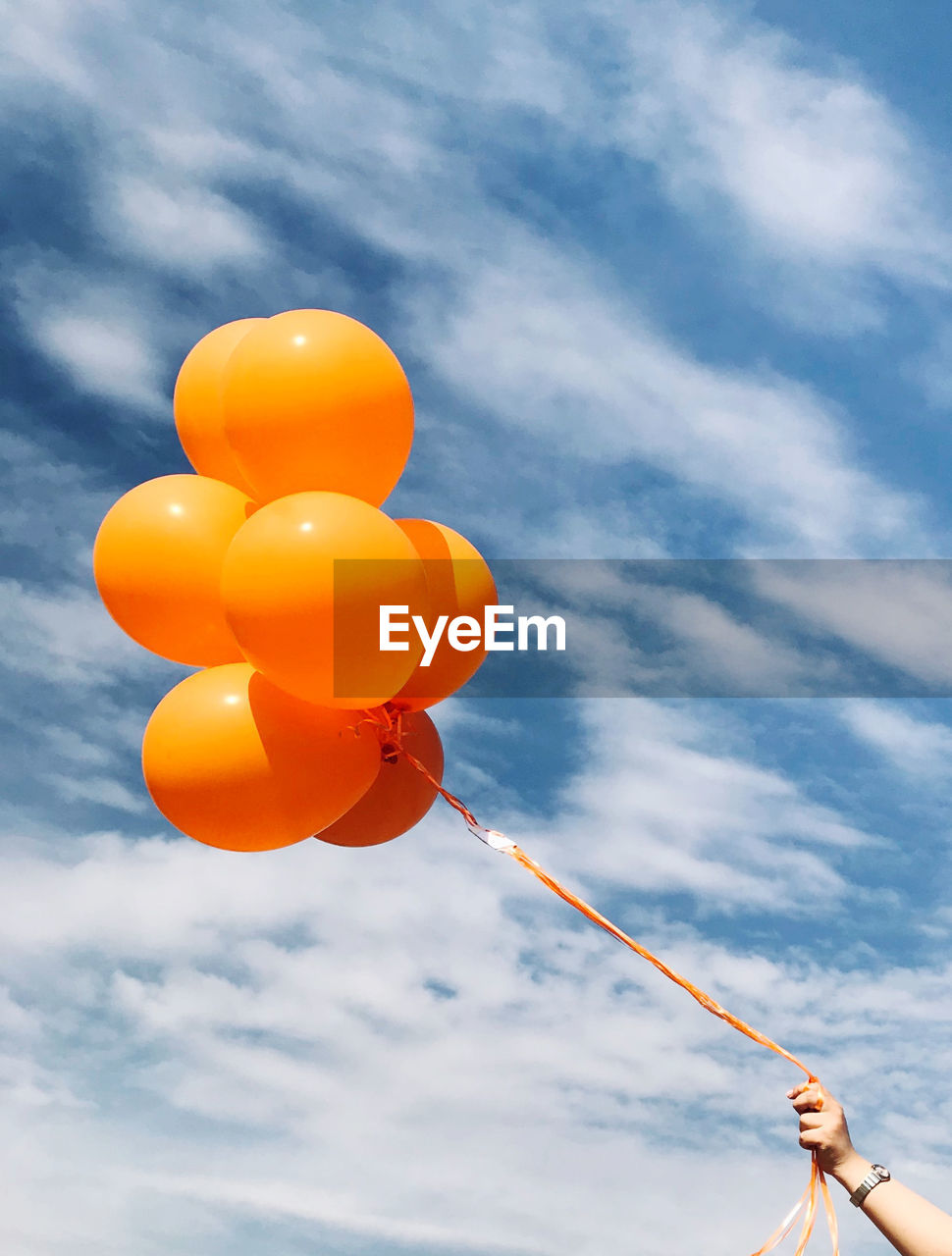 Low angle view of person holding balloons against sky