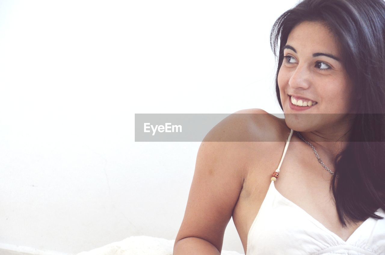 Smiling young woman looking away against wall
