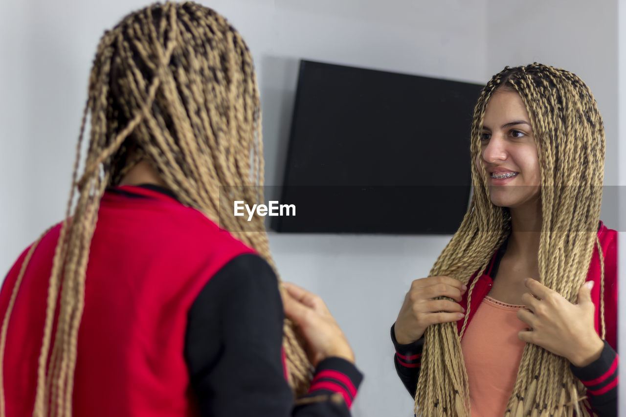 Teen girl standing in front of the mirror admiring the new hairstyle of boxing braids with kanekalon