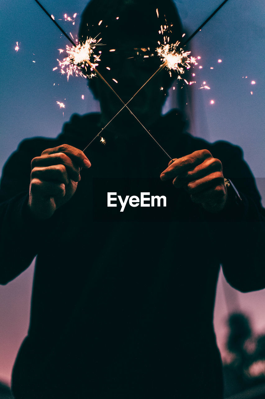 Close-up of man holding illuminated fireworks against sky at night