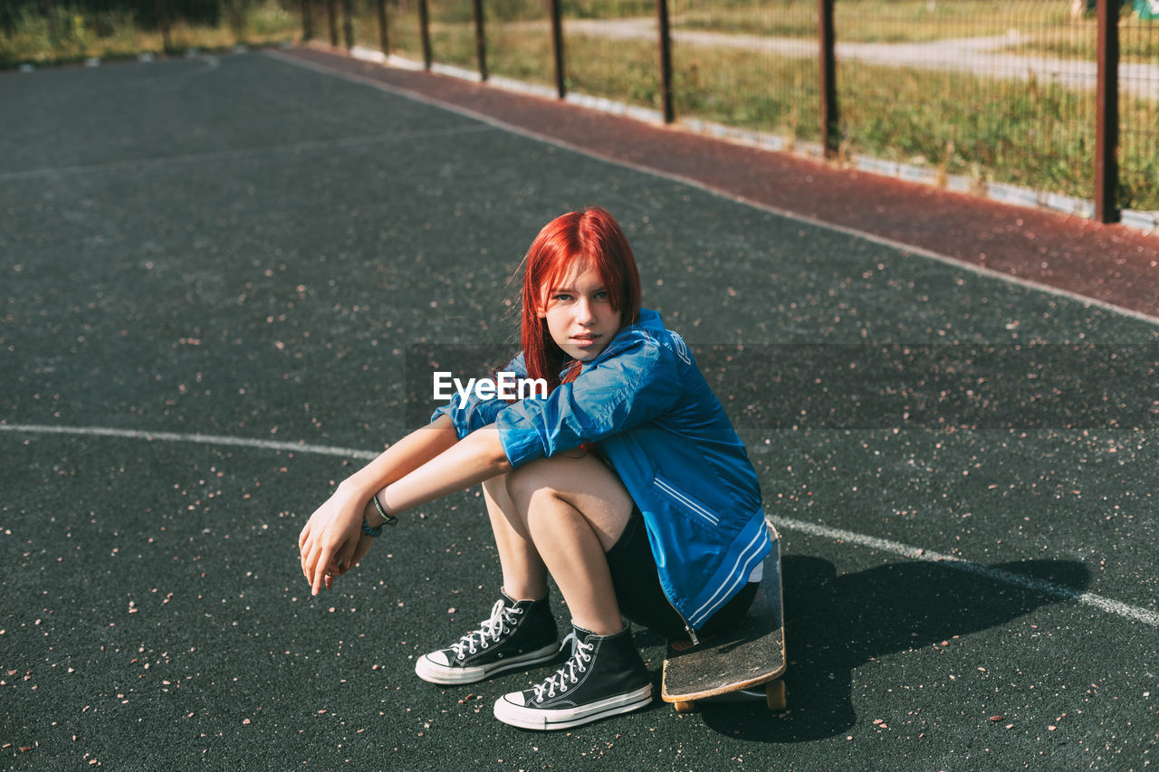 Cute teen girl sitting on a skateboard in the afternoon, outdoors