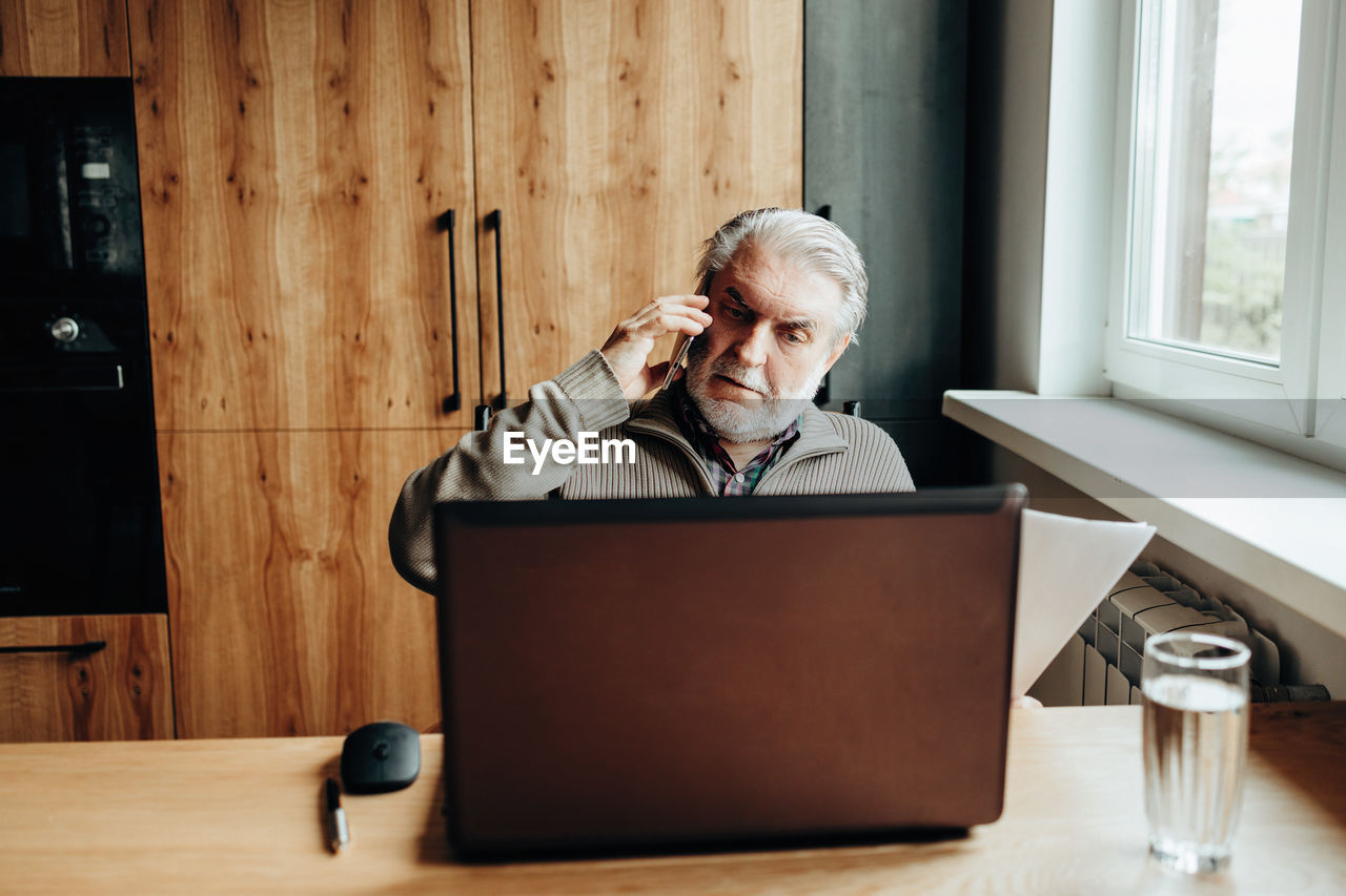 An elderly man works at a laptop, learning from home, home bookkeeping