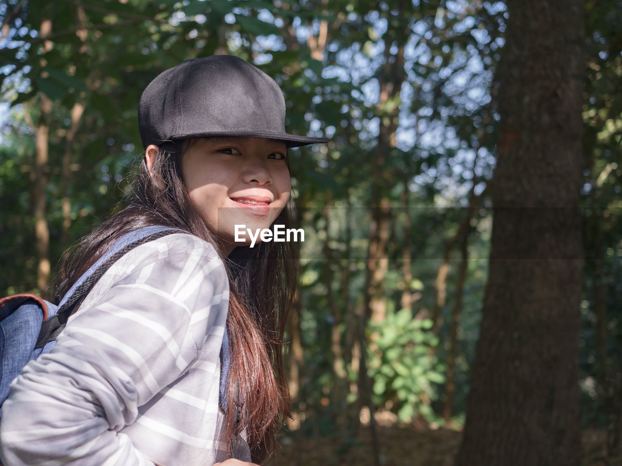 Happy young asian woman with backpack walking on path in summer forest.