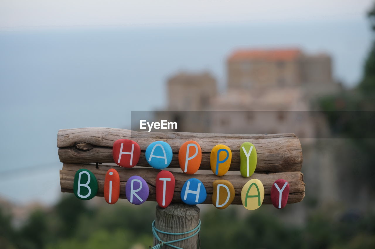 Happy birthday text composed with multi colored stone letters on wood with old village on the back 