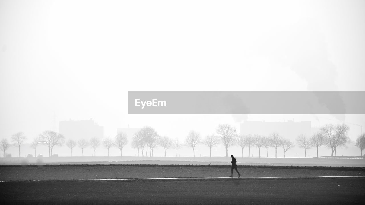 Man walking on field against foggy weather
