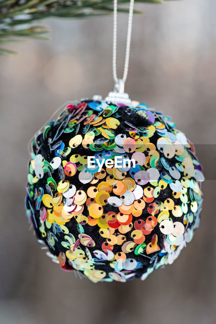 Hanging multi colored glitter christmas ball on spruce and over blurred background