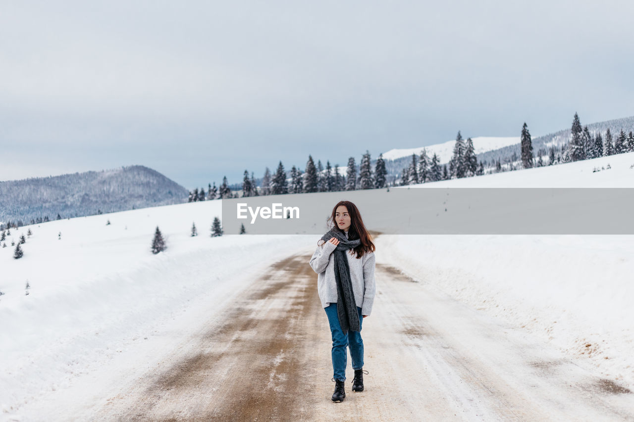 Woman walking on a road cover with snow while on a road trip in the mountains.