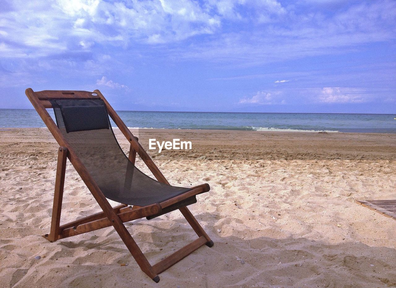 Deck chair on sand against sea