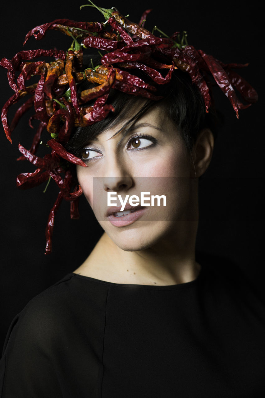 Close-up of young woman wearing red chili peppers against black background