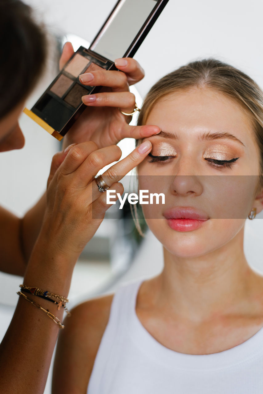 Makeup artist makes up a woman by applying eye shadow to her skin