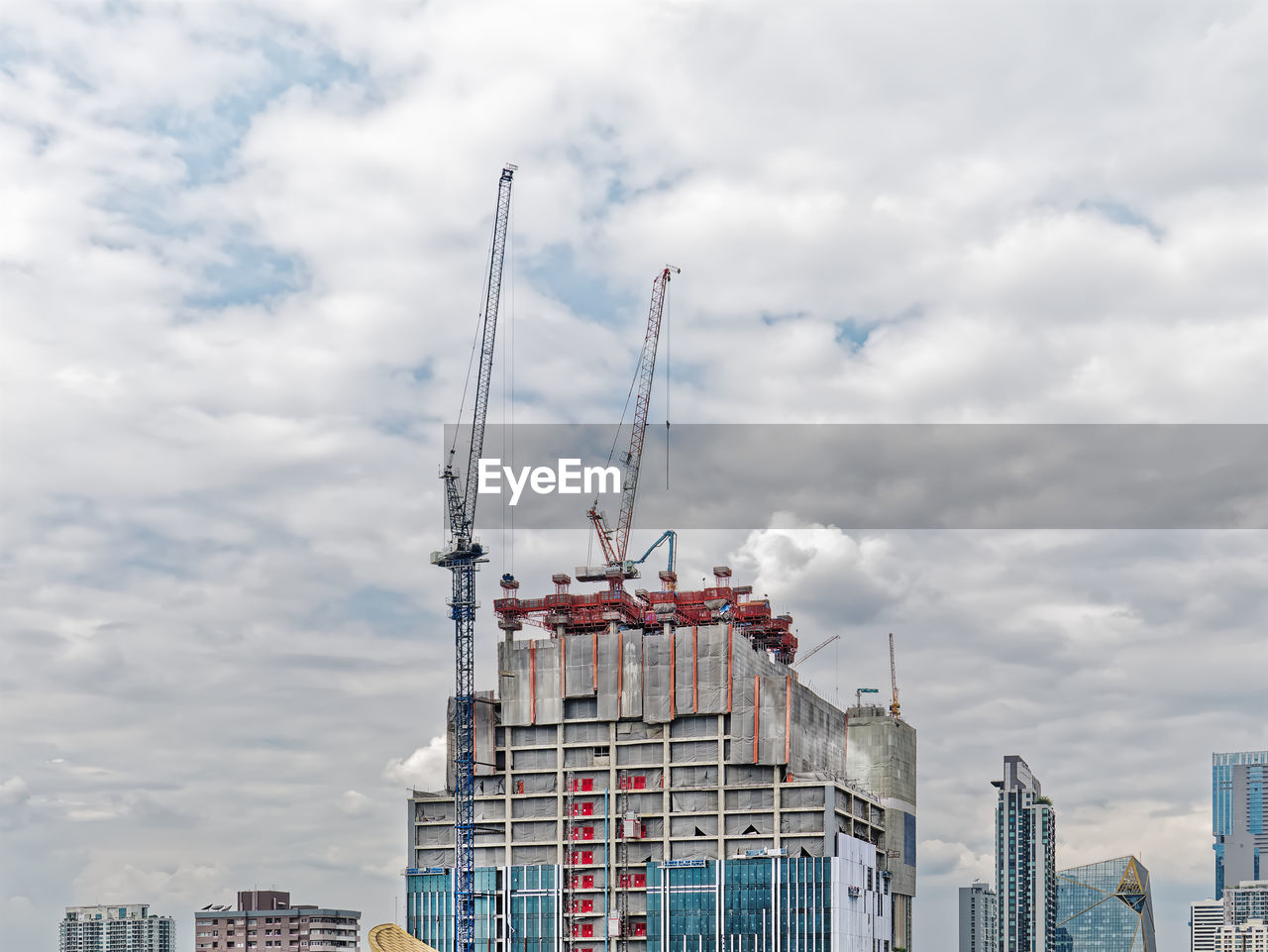 Under construction building with cranes against cloudy sky