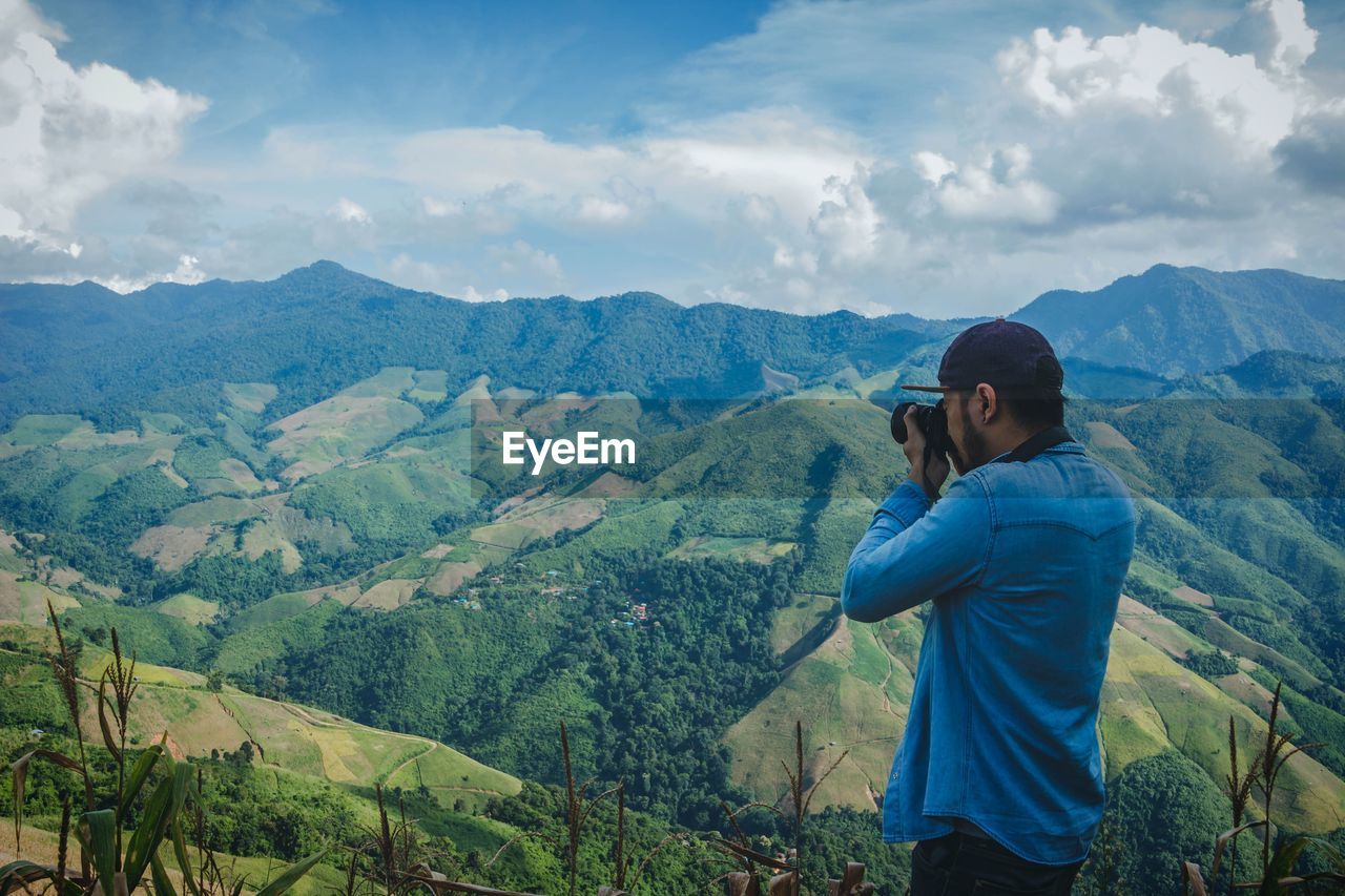 Man photographing mountains against cloudy sky