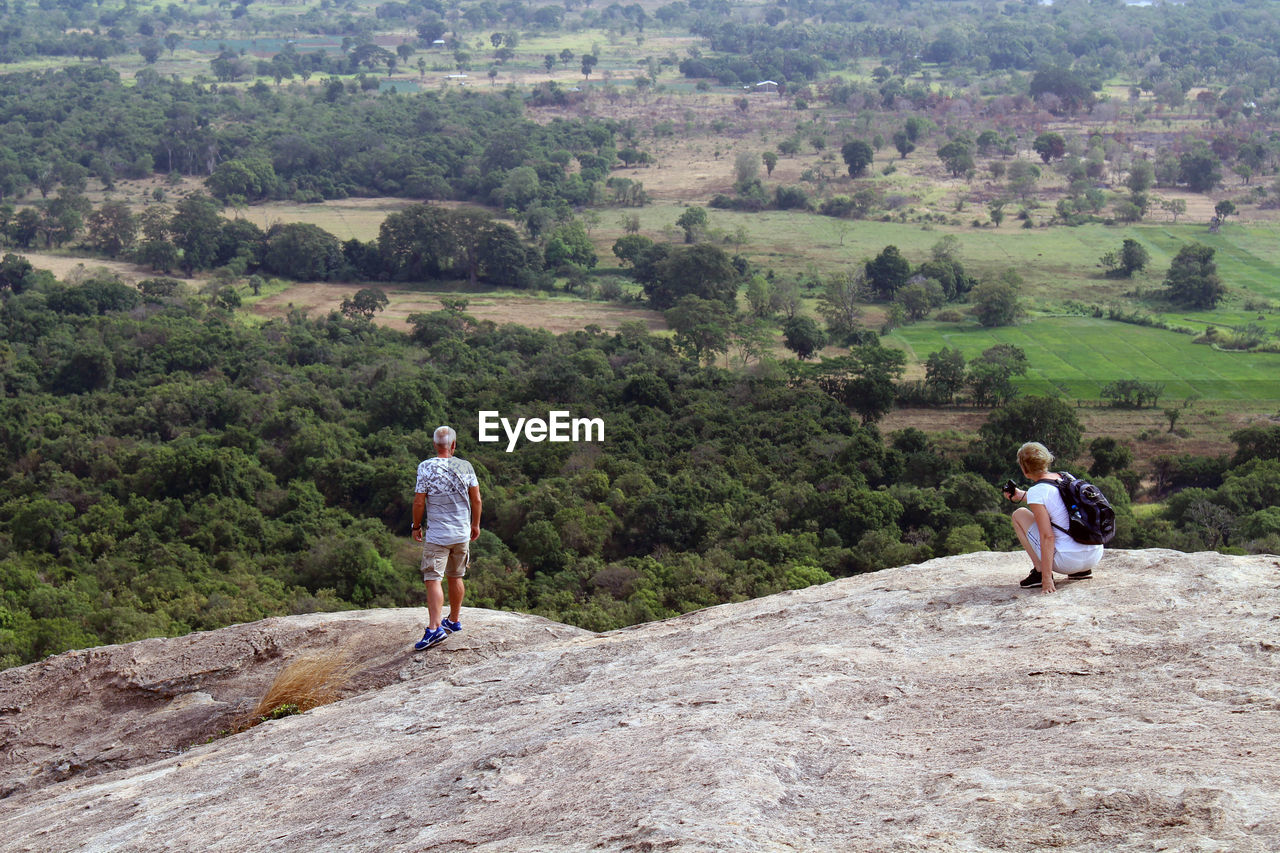 REAR VIEW OF PEOPLE ON ROCK AGAINST TREES