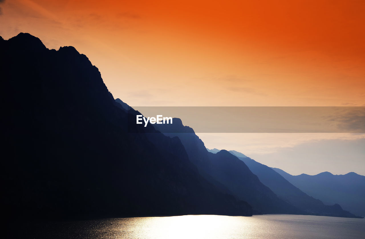 Silhouette mountain by sea against sky during sunset