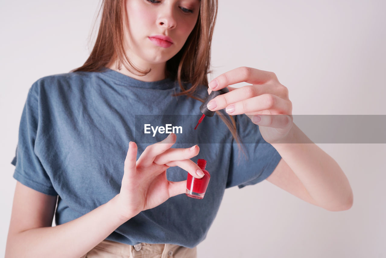 Young woman applying nail polish against wall