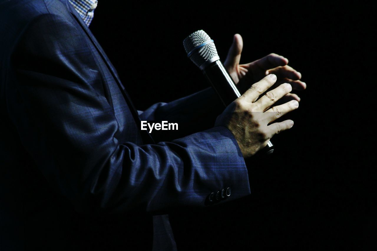 Midsection of businessman holding microphone while standing against black background