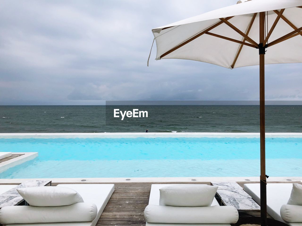 Lounge chairs on floorboard by sea against sky