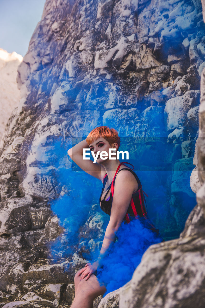 LOW ANGLE VIEW OF YOUNG WOMAN ON ROCK