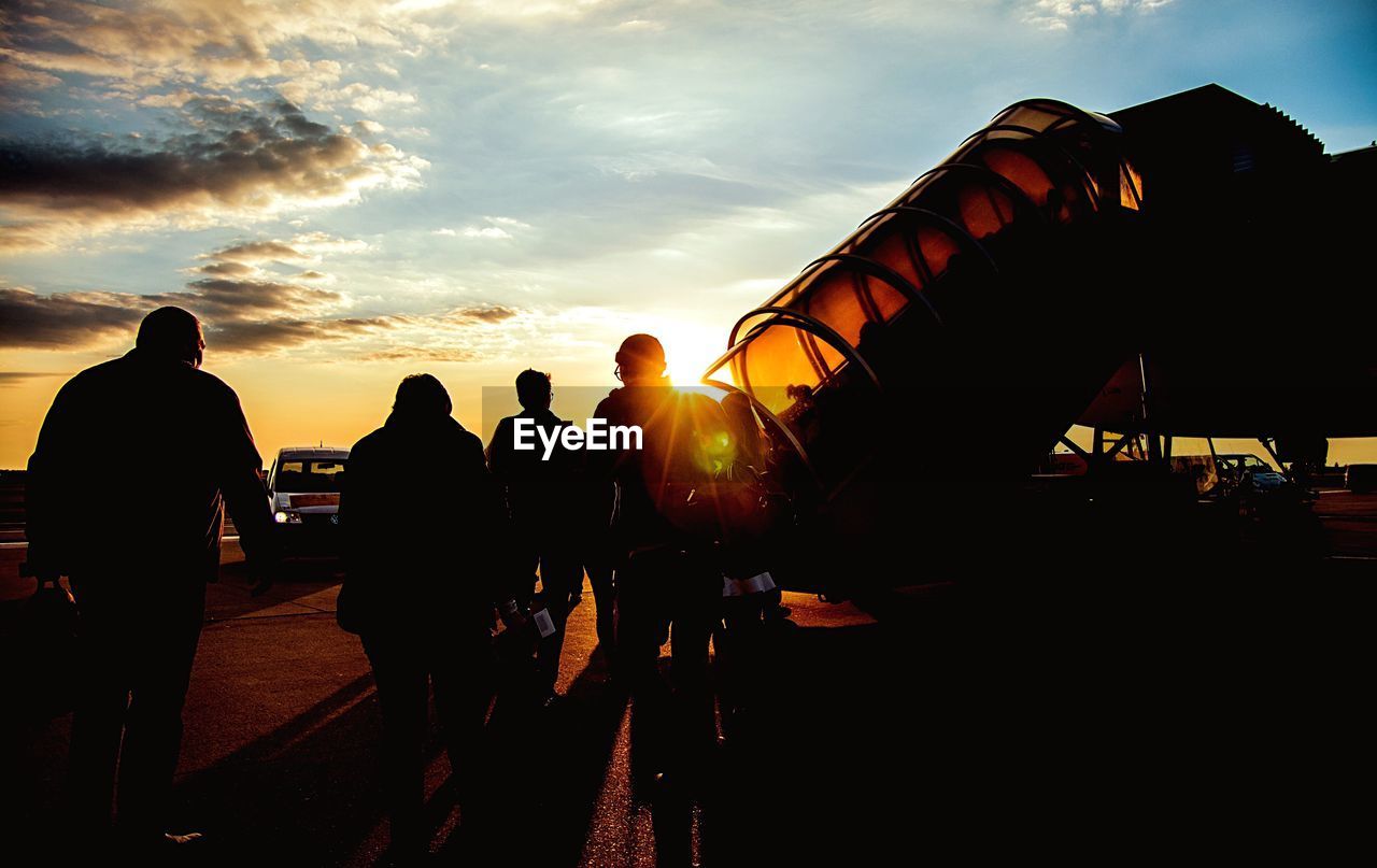 Silhouette people outside airport against sky during sunset