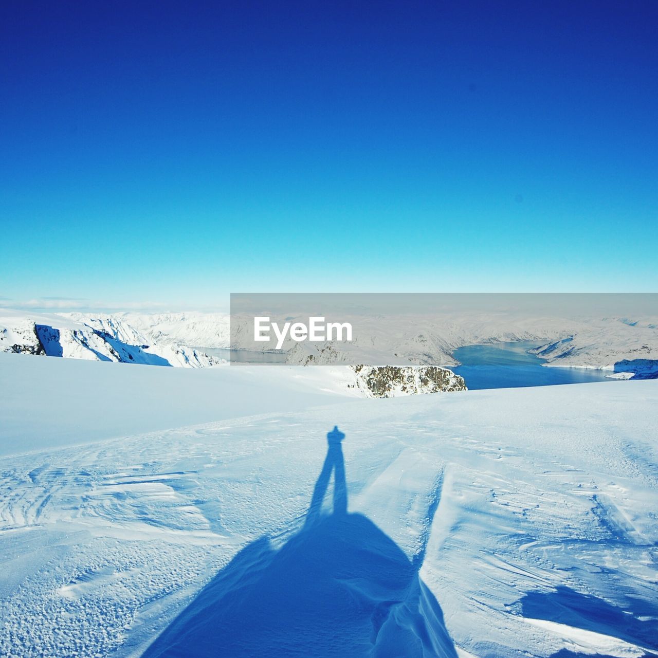 Shadow of man standing on snow covered landscape against clear blue sky